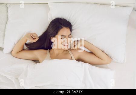 Jeune et belle femme s'étire sur son lit blanc-neige tôt le matin. Banque D'Images