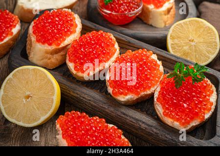 Sandwiches avec caviar rouge, beurre, persil et citron sur fond de bois. Banque D'Images