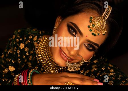 Femme visage portrait en gros plan.Jeune femme modèle à sari regardant l'appareil photo.Porter des bracelets verts et des bijoux.Arrière-plan noir Banque D'Images