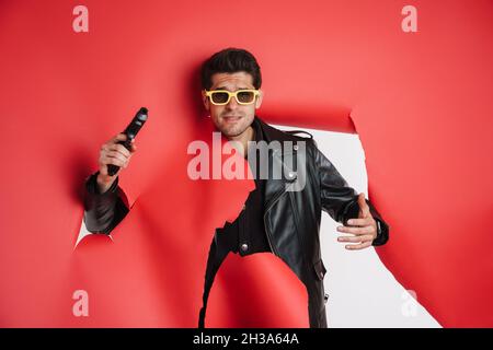 Portrait d'un homme blanc portant une veste en cuir noir, portant un pistolet, piquant hors d'un trou de papier déchiré idéal pour l'action thriller livre couverture desig Banque D'Images