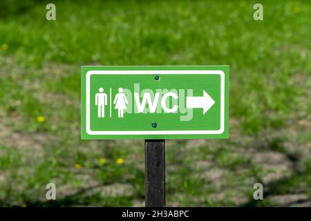 Logo WC, signe des toilettes publiques sur la rue, sur fond d'herbe. Banque D'Images