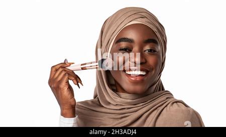 Portrait d'une femme noire musulmane heureuse avec brosse à maquillage Banque D'Images