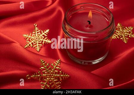 Bougie parfumée rouge avec ornements étoiles de Noël sur fond de tissu en soie rouge vif. Banque D'Images