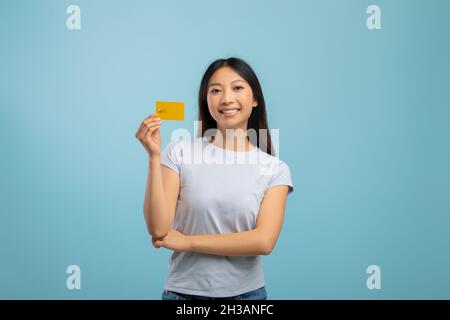 Concept de paiement facile.Bonne jeune femme asiatique tenant la carte de crédit en main et souriant, debout sur fond bleu Banque D'Images