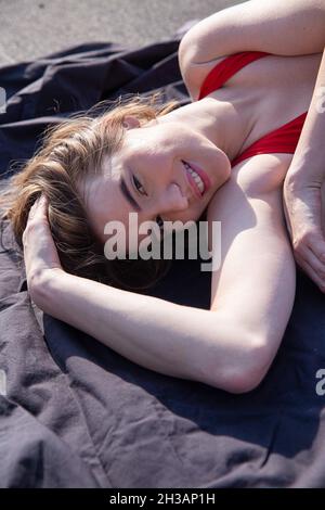 Portrait de la jeune femme caucasienne souriante en maillot de bain rouge allongé sur un tissu noir Banque D'Images