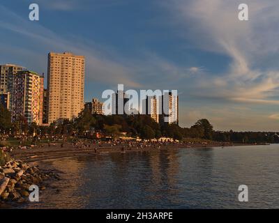 Belle vue sur English Bay Beach dans le quartier de Vancouver West End sur la rive de l'océan pacifique avec des gens qui profitent du coucher du soleil et des bâtiments. Banque D'Images