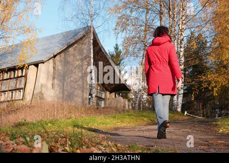 Une femme dans une veste rouge marche à travers le parc d'automne parmi les feuilles mortes jaunes. Banque D'Images