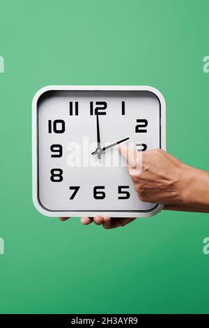 gros plan d'un jeune homme caucasien qui a mis une horloge en arrière, à la fin de l'heure d'été, sur un fond vert Banque D'Images