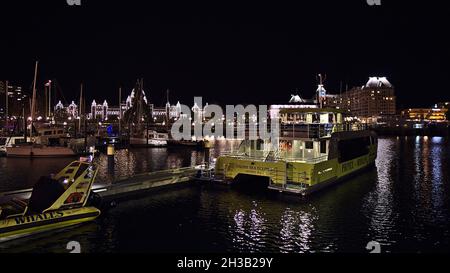 Magnifique vue nocturne sur le port intérieur de Victoria avec bateaux d'observation des baleines et bâtiments du Parlement illuminés avec reflets d'eau. Banque D'Images