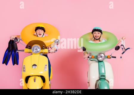 Photo d'un couple mature heureux et excité en voiture de casque mobylette avec bouée vacances d'été isolé sur fond rose Banque D'Images