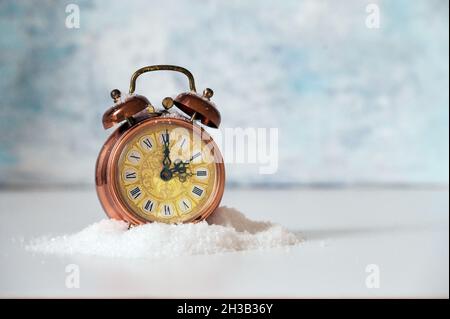 Vintage alarm clock in artificial snow showing clock change to winter time, light blue background with copy space, selected focus, narrow depth of fie Banque D'Images