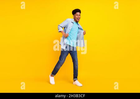 Photo de drôle cool peau sombre gars habillé denim chemise marche danse chant isolé couleur jaune fond Banque D'Images