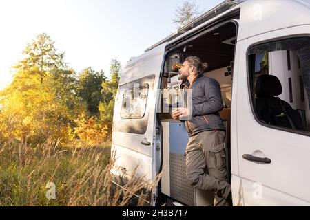 Homme et sa camionnette de camping debout dans un paysage d'automne Banque D'Images