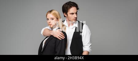 femme blonde avec cigarette regardant la caméra près de l'homme branché embrassant son isolé sur la bannière grise Banque D'Images