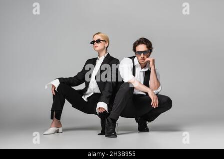 couple élégant en costume noir et lunettes de soleil sombres posé sur le gris Banque D'Images