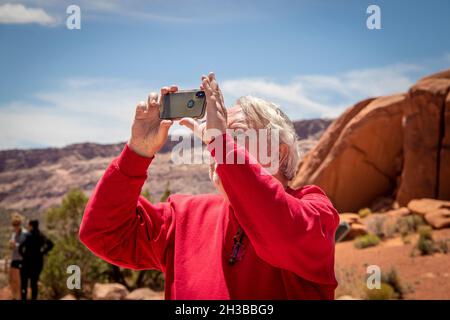 05 23 2021 Arches National Park USA - l'homme senior en chemise rouge prend une photo dans le désert avec un iphone - formation de rocher et d'autres touristes flous Banque D'Images