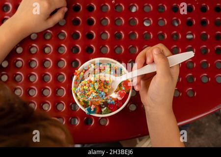 Garçon creusant dans une tasse de papier de glace lyophilisée et de bonbons Banque D'Images