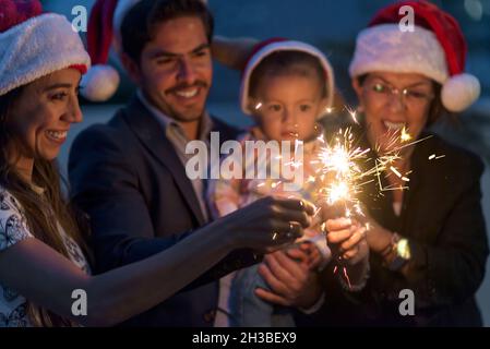 Famille latine célébrant noël nouvel an en s'amusant avec des spamisseurs à l'aube portant des chapeaux de Père Noël Banque D'Images