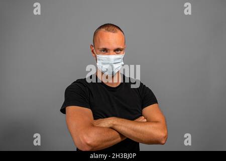 Image d'un homme caucasien gai debout contre le mur gris avec les bras croisés portant un t-shirt noir.Regarder la caméra.Un succès assuré Banque D'Images