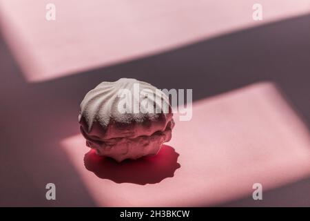 Un guimauve blanc repose sur un fond rose avec des ombres. Banque D'Images