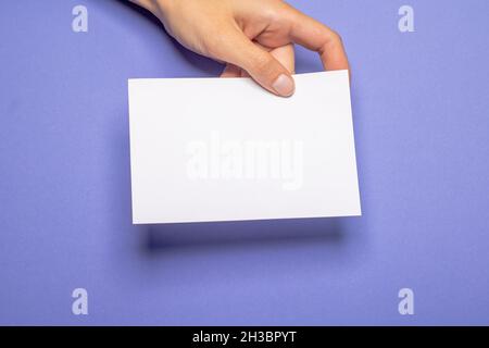 la main femelle tient un morceau de papier vierge avec un espace de copie devant un carton d'arrière-plan violet Banque D'Images