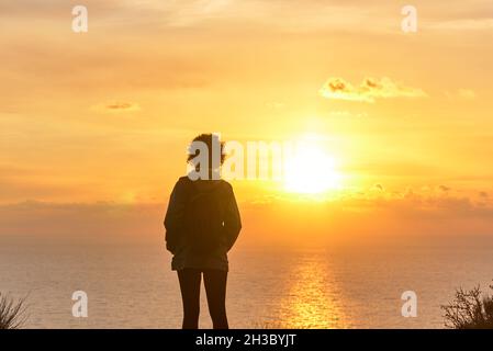 Une femme de randonnée de derrière regardant le lever du soleil sur la mer Banque D'Images