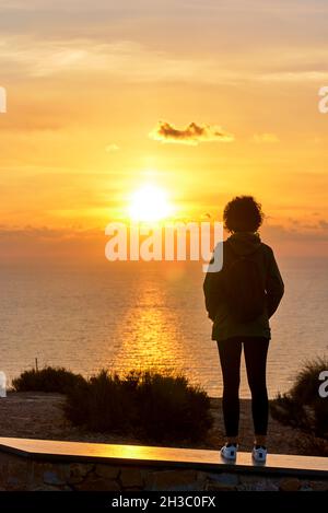 Une femme de randonnée de derrière regardant le lever du soleil sur la mer Banque D'Images