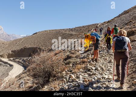 Kagbeni, Mustang District, Népal - 19 novembre 2016 : groupe de touristes se promène le long d'un étroit chemin de montagne.Une femme est devenue malade et se repose. Banque D'Images