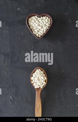 Haricots blancs dans un bol en forme de coeur et cuillère en bois sur fond noir.vue du dessus. Banque D'Images