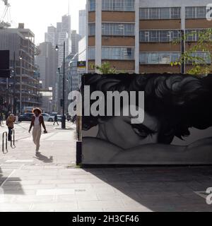 Londres, Grand Londres, Angleterre, octobre 26 2021 : un piéton à la mode passe devant l'art de la rue à Shoreditch avec des gratte-ciels en arrière-plan. Banque D'Images