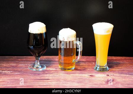 Trois verres de différentes formes avec différentes variétés de bières claires, de blé et foncées se tiennent sur une table en bois.Gros plan. Banque D'Images