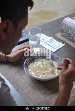 Un jeune homme asiatique mangeant du thenthuk (cousin tibétain) dans un café tibétain Banque D'Images