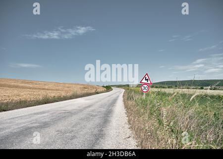 Route de gravier et magnifiques champs agricoles de baies de blé jaune près de la route et du panneau de signalisation Banque D'Images