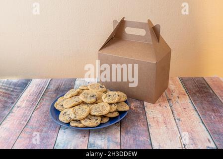 biscuits aux flocons d'avoine fourrés de chocolat et de fruits sur une assiette bleue et boîte en carton à emporter sur une table en bois Banque D'Images