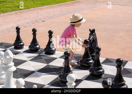 Petite fille caucasienne jouant des échecs géants dans le parc, photographie horizontale.Une fille qui fait un mouvement de pion Banque D'Images