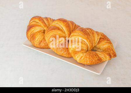 Plateau avec trois croissants au beurre pour le petit déjeuner sur table blanche Banque D'Images