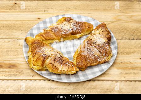 Délicieux croissants au beurre avec des tranches d'amandes, du sirop et du sucre glace sur une table en bois brut Banque D'Images