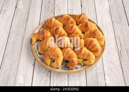 Assiette bleue bordée d'or remplie de mini croissants au beurre sur une table en bois clair Banque D'Images