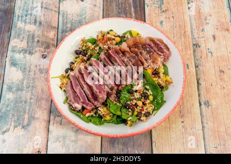 Filet de bœuf haché cuit au point sur une salade d'épinards, du riz, des haricots et des légumes avec des flocons de sel de mer Banque D'Images