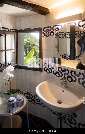 Petite salle de bains avec lavabo et miroir rond.Il y a une table basse avec une orchidée et deux vases.Fenêtre lumineuse.Personne à l'intérieur Banque D'Images