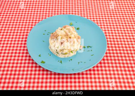 Assiette de salade russe aux olives avec mayonnaise, œufs durs et thon en conserve avec persil sur nappe blanche et rouge Banque D'Images