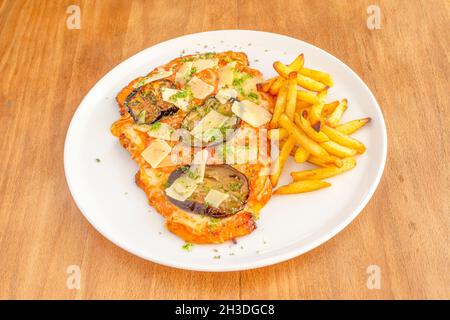 Schnitzel de veau argentin au fromage mozzarella, tranches de parmesan, sauce au pesto, aubergines, tranches de tomates et une garniture de chips maison Banque D'Images