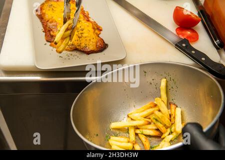 Le chef assemble une assiette de milanesa de veau avec une garniture de frites maison Banque D'Images