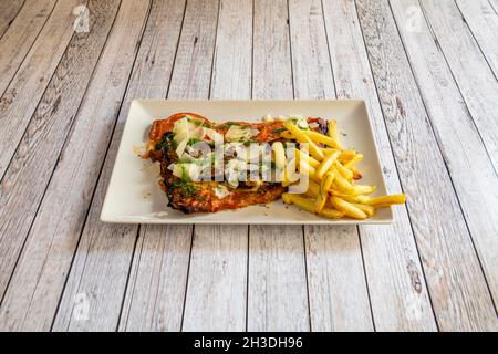 Schnitzel méditerranéen avec tranches de parmesan et sauce pesto, aubergines, tomates et frites Banque D'Images