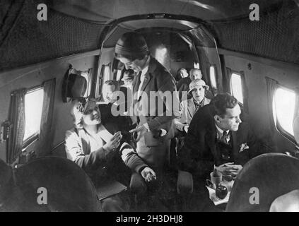 Compagnie aérienne voyageant dans les années 1930.Un groupe de femmes et d'hommes dans un avion américain de passagers dans les années 1930.La femme de bord est debout au milieu de l'avion pour desservir une jeune femme. Banque D'Images