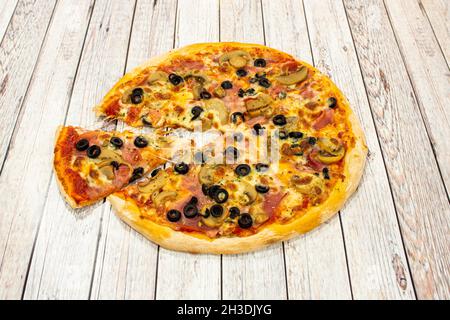 Petite pizza à croûte mince avec des tranches d'olives noires, des tranches de champignons, du jambon cuit, de l'origan et une portion qui étire le fromage mozzarella fondu Banque D'Images