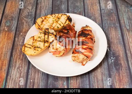 petits pains de poulet farcis au fromage et au jambon, enveloppés de tranches de bacon frites, garnis de pommes de terre au barbecue avec sauce à l'ail et au persil Banque D'Images