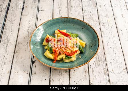 raviolis farcis à la viande avec morceaux de bacon fumé, feuilles de basilic et tomates déshydratées dans un bol bleu Banque D'Images