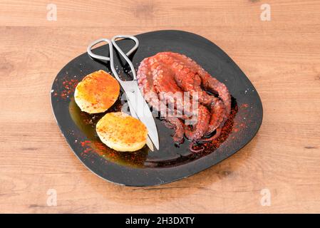 Poulpe cuite galicienne avec des pommes de terre, de l'huile d'olive, du paprika de la Vera et du sel de mer avec des ciseaux de poisson pour les hacher Banque D'Images