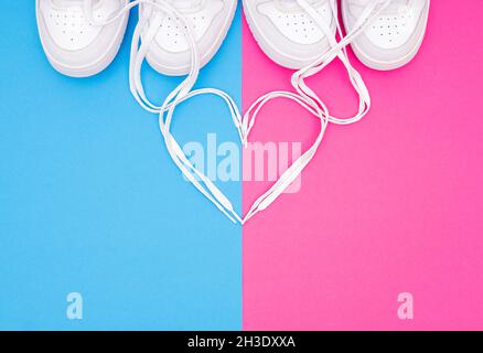 Une vue rognée des sneakers blanches assorties et d'une forme de coeur faite des lacets sur un fond vif.Concept romantique pour les couples portant une chaussure assortie Banque D'Images